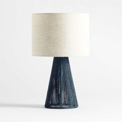 A modern coastal table lamp featuring a conical base wrapped in woven deep navy blue rope, topped with a textured beige linen drum shade on a plain white background.