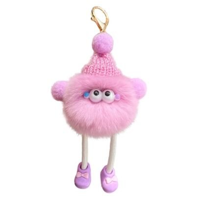 A cute fluffy pink plush monster keychain wearing a knitted pink beanie with a pom-pom, featuring big cartoon eyes, tiny plush hands, long cord legs, and purple shoes with bows, attached to a gold clip against a plain white background.