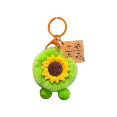 A cute fluffy bright green plush pom-pom keychain featuring a cheerful yellow sunflower face, two small green plush feet, an orange key ring clip, and a kraft paper tag reading "Take the first place" against a clean white background.