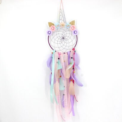 A whimsical handmade unicorn dream catcher with a floral crown, silver horn, lace ribbons, and purple and peach feathers, hanging against a white wall.